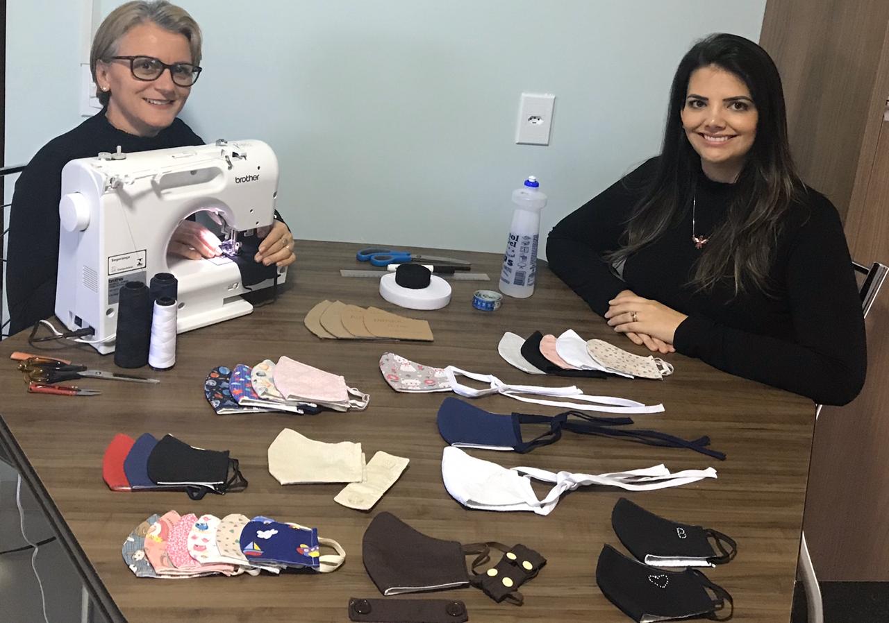 Elisa Ortigara e B&aacute;rbara Gaio com a m&aacute;quina de costura nova, adquirida com a venda das m&aacute;scaras